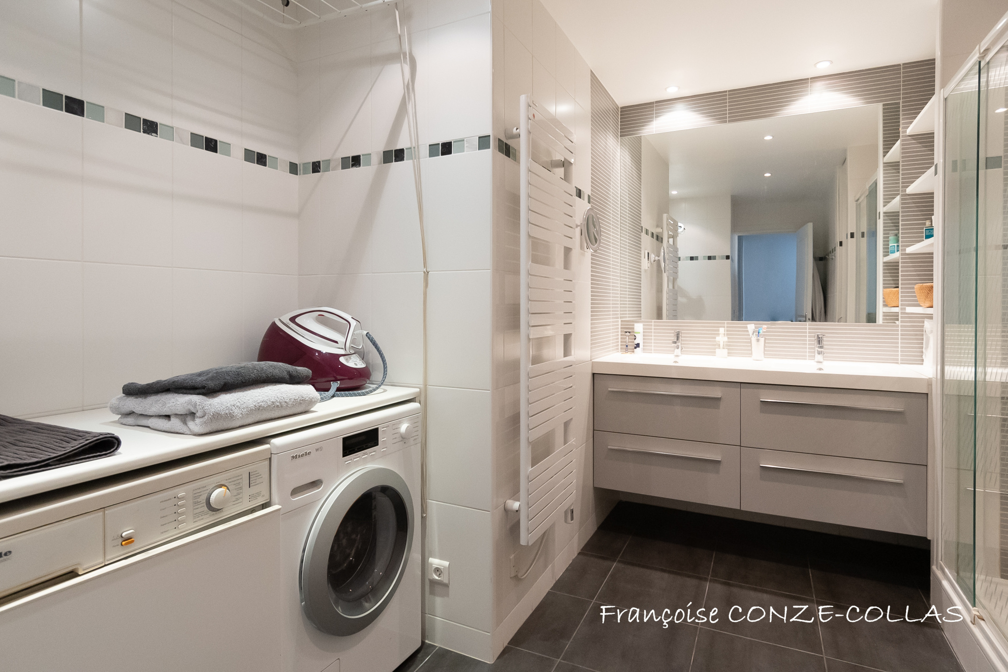 Salle de bain moderne avec machine à laver et lavabo, carrelage gris et murs blancs.