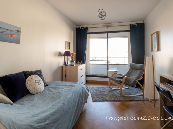 Chambre lumineuse avec fauteuil et lit, accès à un balcon, décorée sobrement.