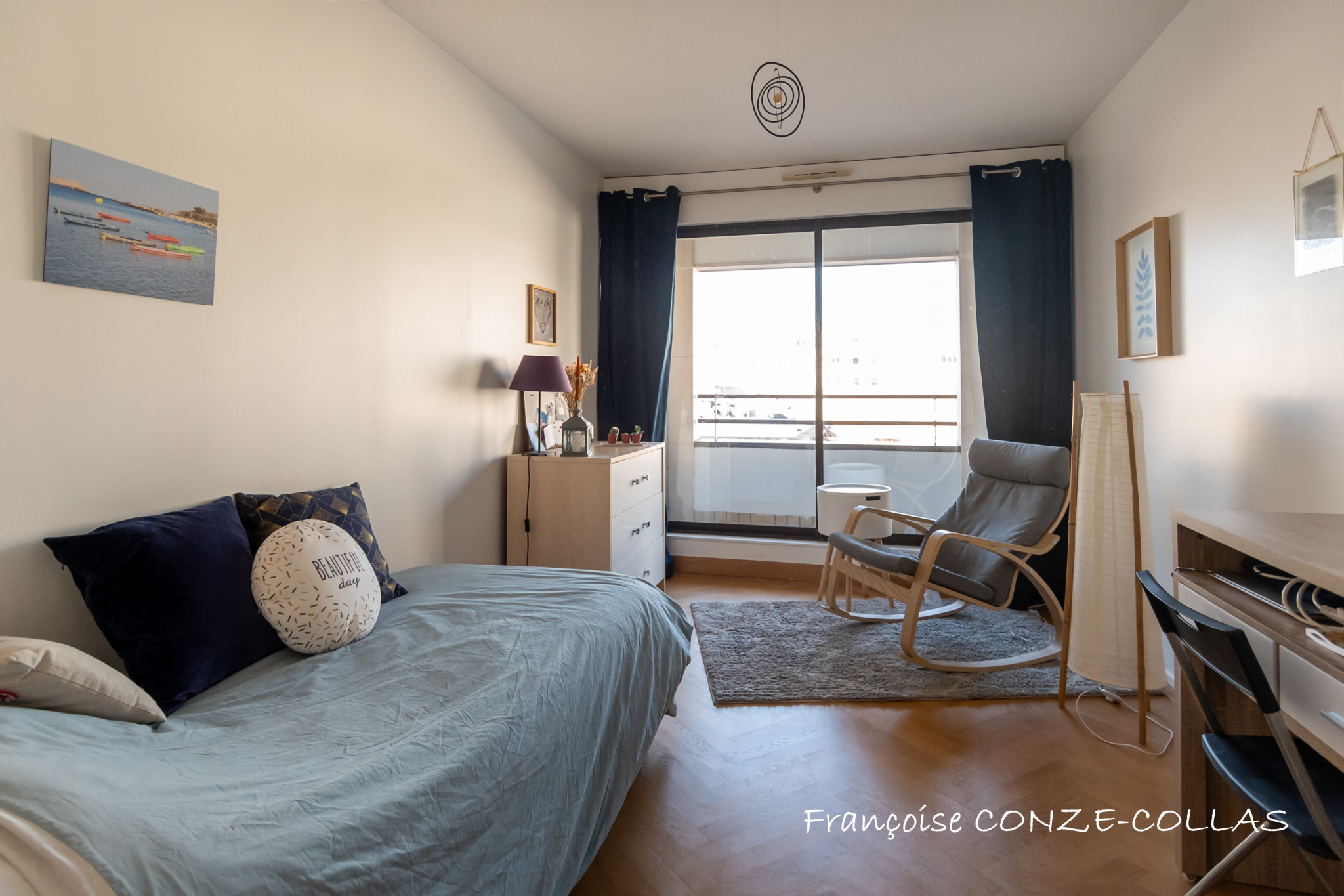 Chambre lumineuse avec fauteuil et lit, accès à un balcon, décorée sobrement.