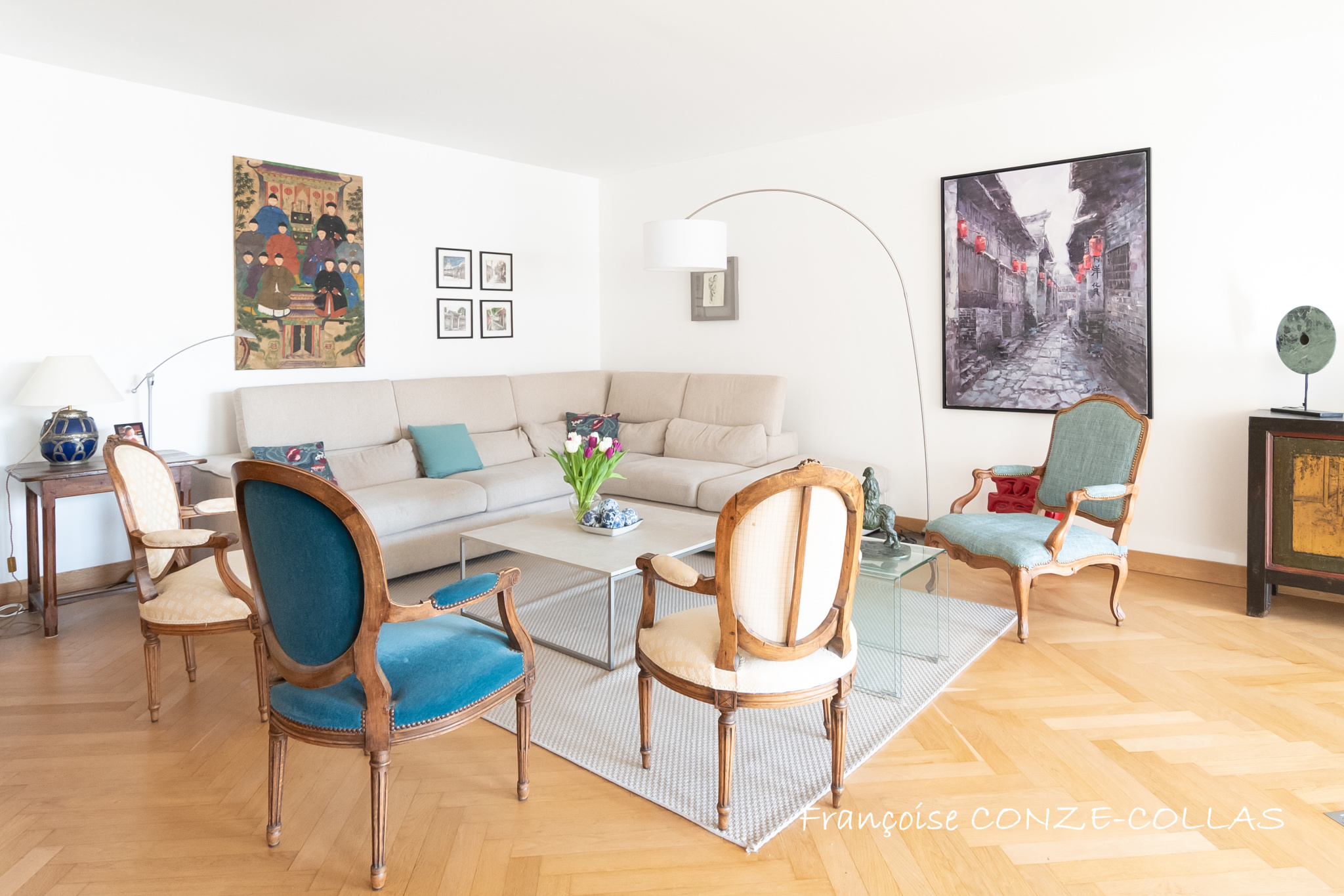 Salon lumineux d'un appartement familial avec canapé, table en verre et chaises anciennes.