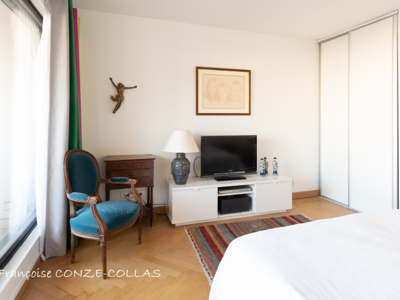 Chambre d'un appartement lumineux avec télévision, fauteuil et décoration simple.