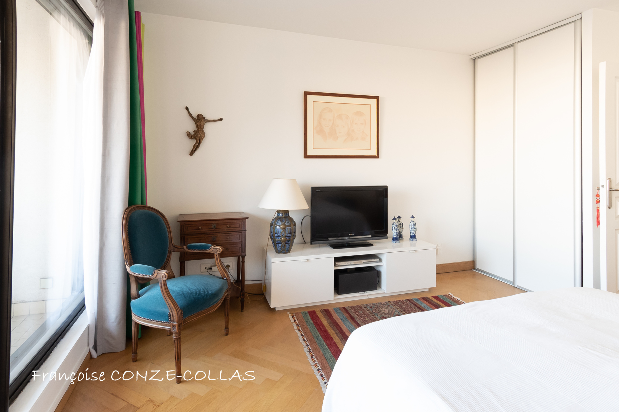 Chambre d'un appartement lumineux avec télévision, fauteuil et décoration simple.
