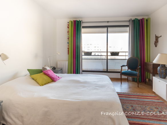 Chambre lumineuse avec un lit double et un accès à un balcon, décoration colorée.