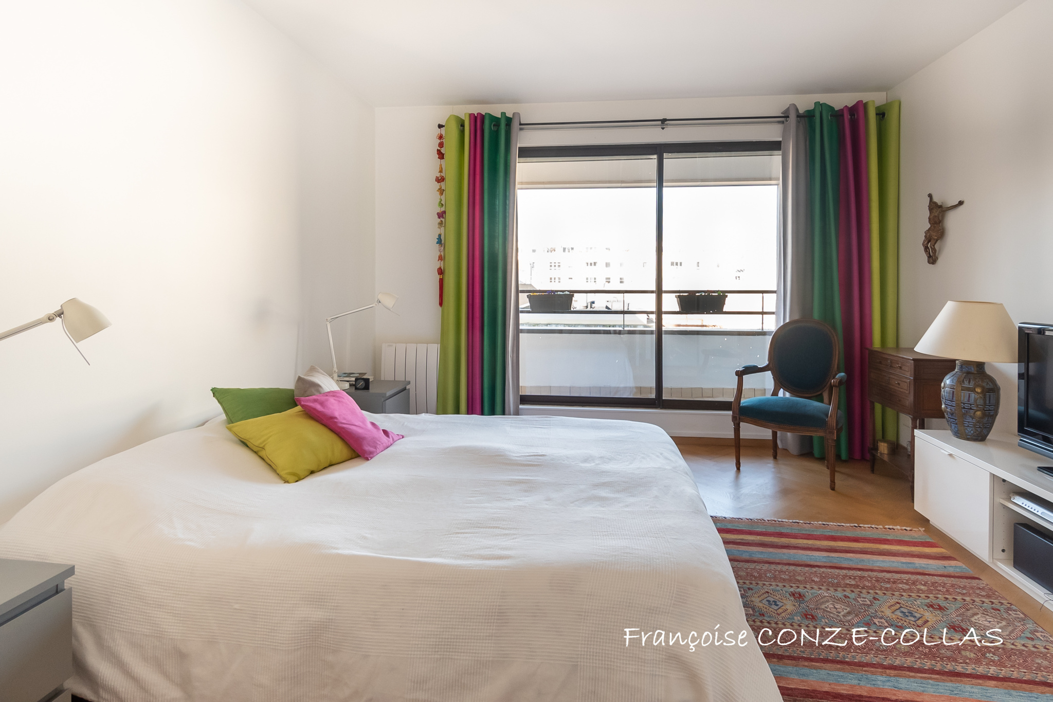 Chambre lumineuse avec un lit double et un accès à un balcon, décoration colorée.