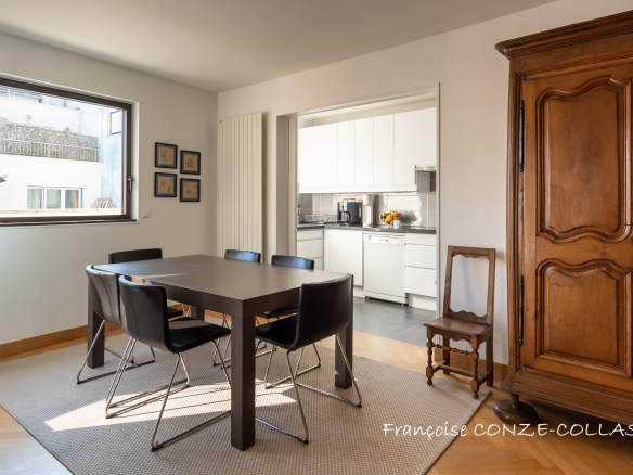 Salle à manger d'un appartement lumineux avec table et chaises, vue sur la cuisine.