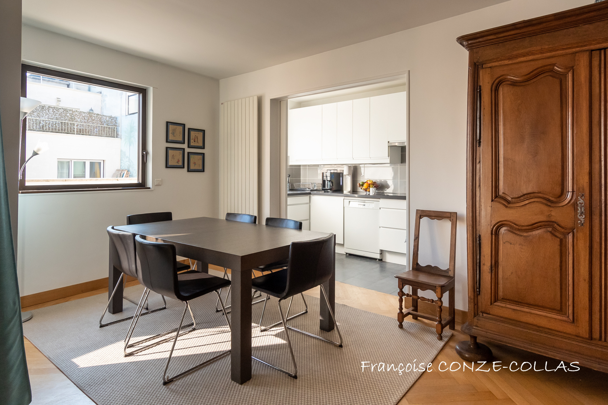 Salle à manger d'un appartement lumineux avec table et chaises, vue sur la cuisine.