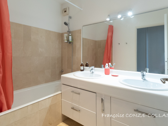 Salle de bain moderne avec baignoire et double vasque, murs en carrelage beige.