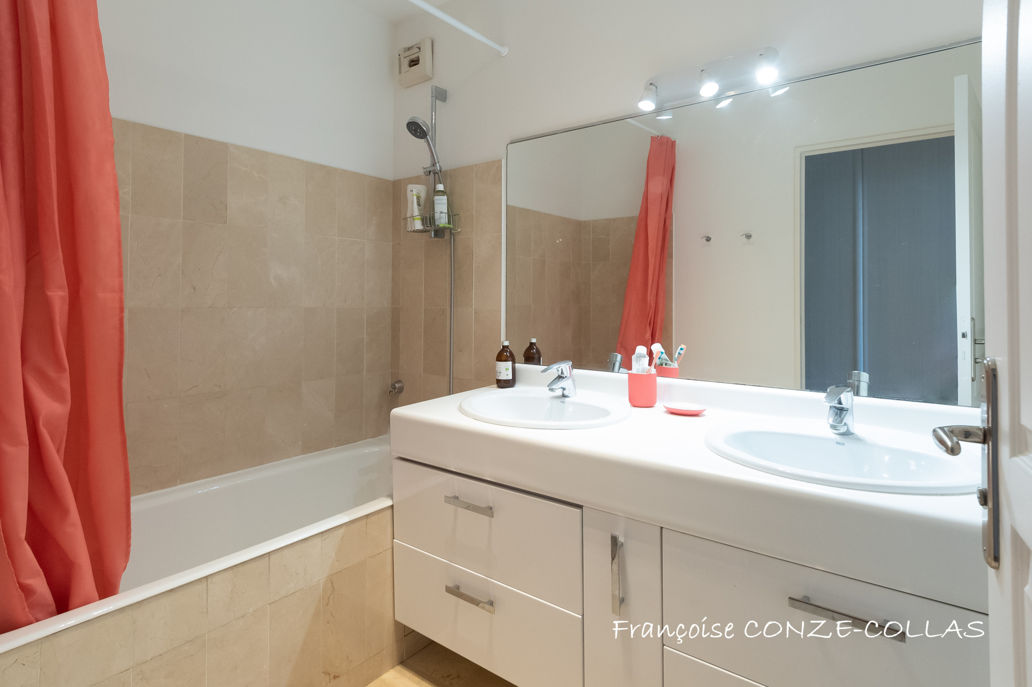 Salle de bain moderne avec baignoire et double vasque, murs en carrelage beige.