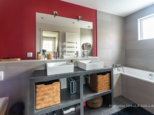 Salle de bain moderne avec deux lavabos et baignoire, murs gris et rouge.