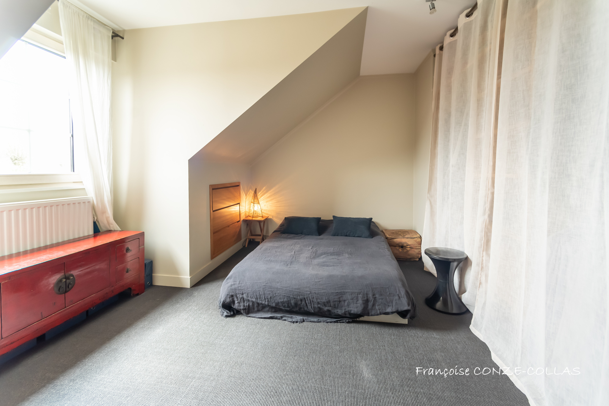 Chambre moderne et lumineuse Chambre avec lit au sol, décorée sobrement, murs inclinés et fenêtre laissant entrer la lumière.