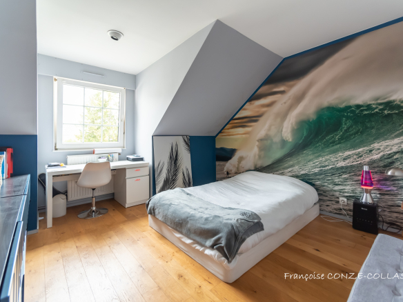 Chambre d'une maison avec décor mural représentant une vague, bureau et lit.
