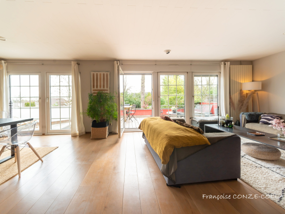 Intérieur d'une maison moderne avec salon lumineux, grandes fenêtres et accès à une terrasse.