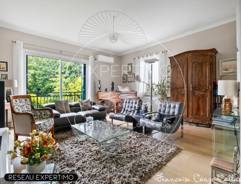 Salon d’une maison à vendre à Marnes-la-Coquette Salon lumineux avec canapé et piano, fenêtres donnant sur un jardin verdoyant.
