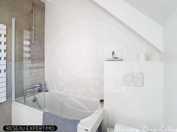 Salle de bain moderne avec baignoire et douche, murs clairs et fenêtre.