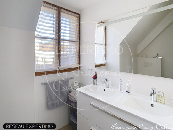 Salle de bains moderne avec lavabo et miroir, fenêtres laissant entrer la lumière.