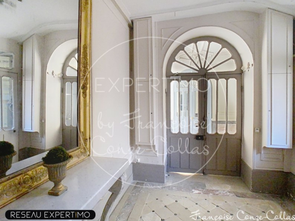 Entrée d'un appartement dans un immeuble ancien avec miroir et portes en bois.