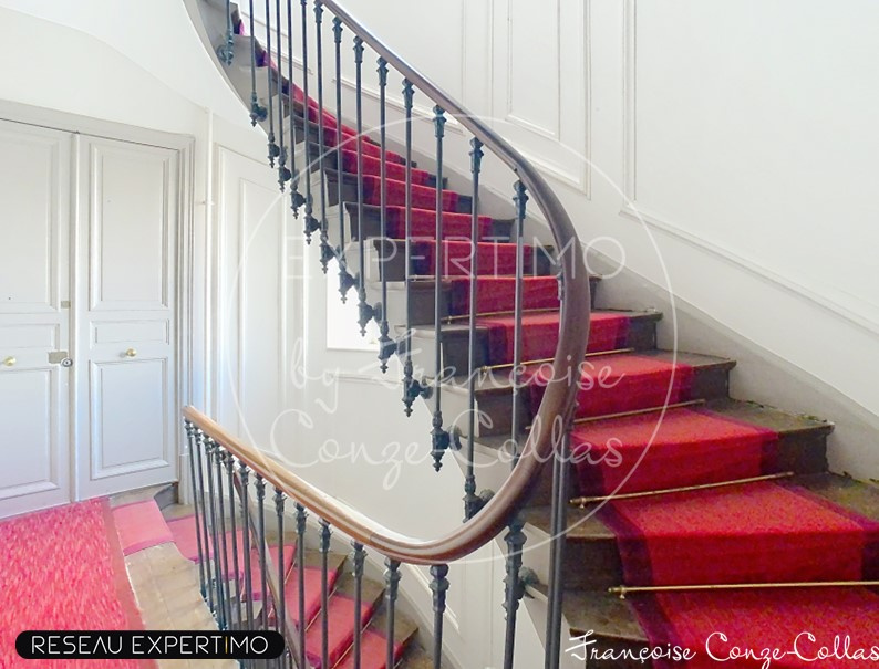 Escalier d’un appartement à Versailles Escalier en colimaçon avec rampe en fer forgé et moquette rouge dans un immeuble ancien.