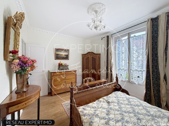 Room with wooden bed, antique wardrobe and windows overlooking a garden.