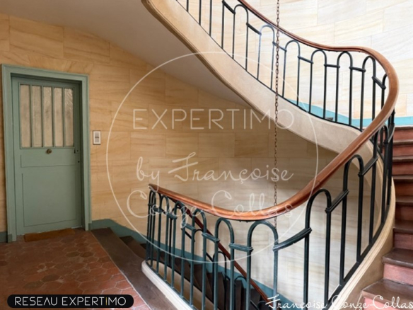 Escalier intérieur d'un immeuble ancien avec rampe en fer forgé et murs en pierre.