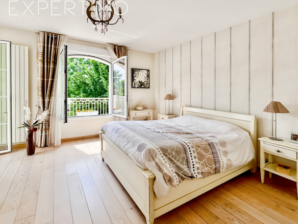 Chambre lumineuse avec lit double et accès à un balcon, décorée avec des murs en bois et un sol en parquet.