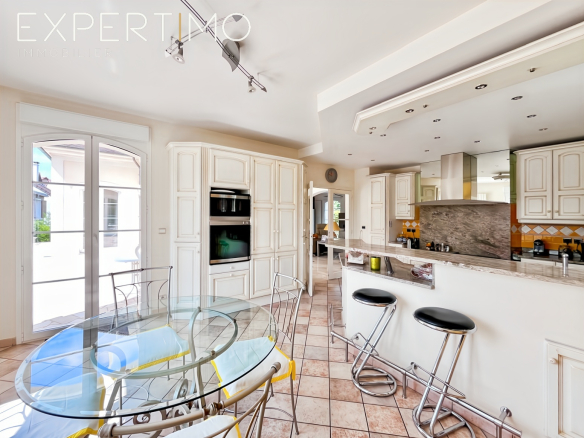 Cuisine moderne avec table en verre et chaises en métal, ouverte sur un espace lumineux.