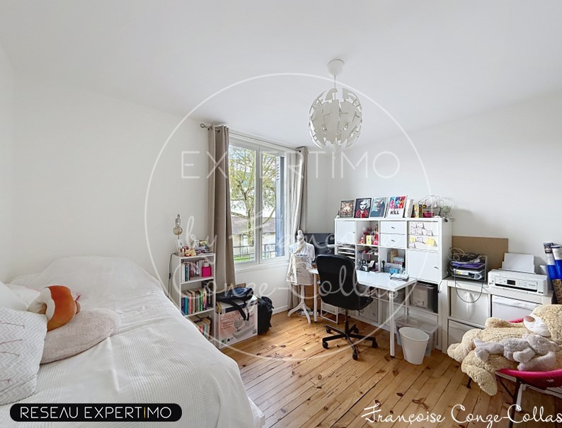 Chambre lumineuse avec un bureau et des rangements, fenêtres donnant sur l'extérieur.