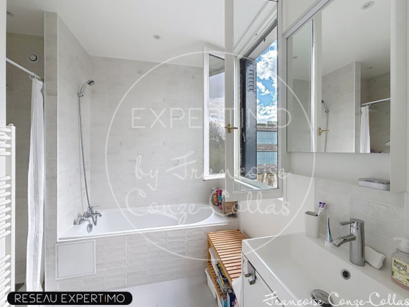 Salle de bain moderne avec baignoire et lavabo, lumière naturelle par fenêtre.
