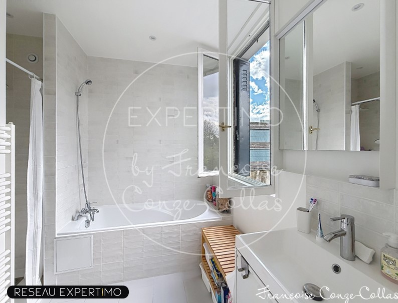 Salle de bain moderne avec baignoire et lavabo, lumière naturelle par fenêtre.