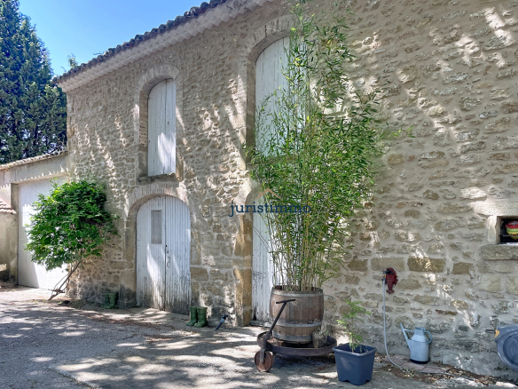 Stone building with wooden shutters and surrounding vegetation, located in a wooded park.