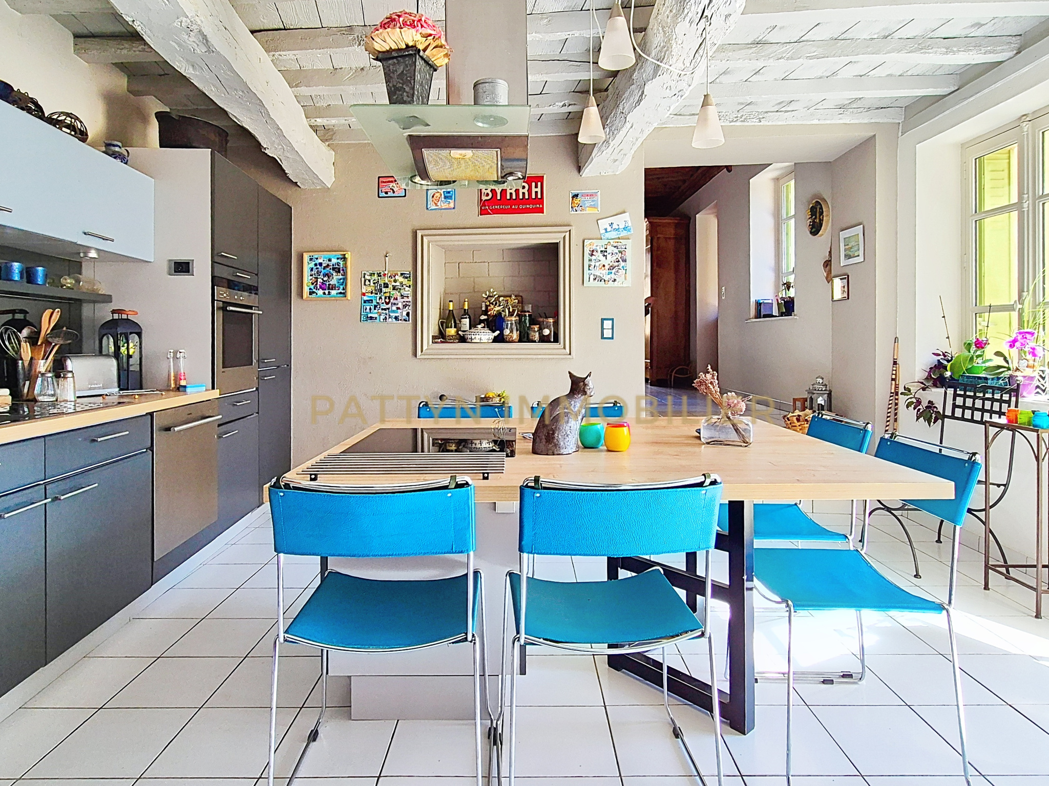 Modern cuisine in Tramoyes Interior of a modern kitchen with a wooden table and blue chairs, decorated with photos and objects.