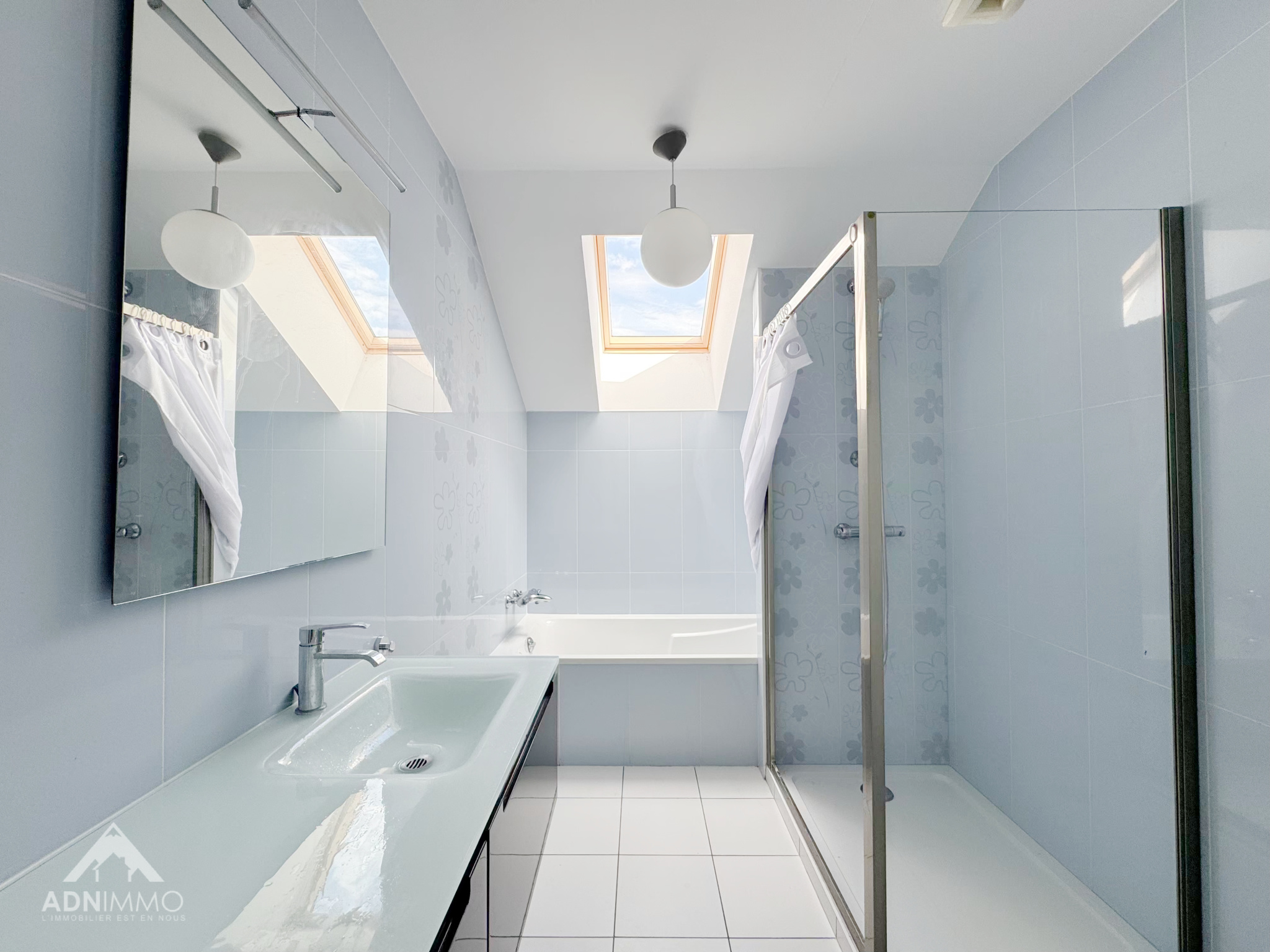 Salle de bain moderne avec baignoire et douche, fenêtres de toit.