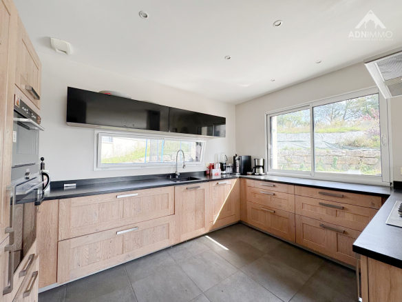 Cuisine moderne avec meubles en bois et plan de travail noir, lumineuse, fenêtres sur le jardin.