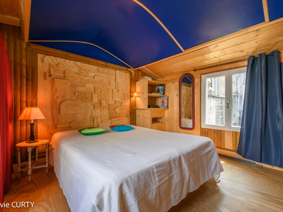 Chambre avec lit double, mur en bois et plafond bleu, fenêtres donnant sur l'extérieur.