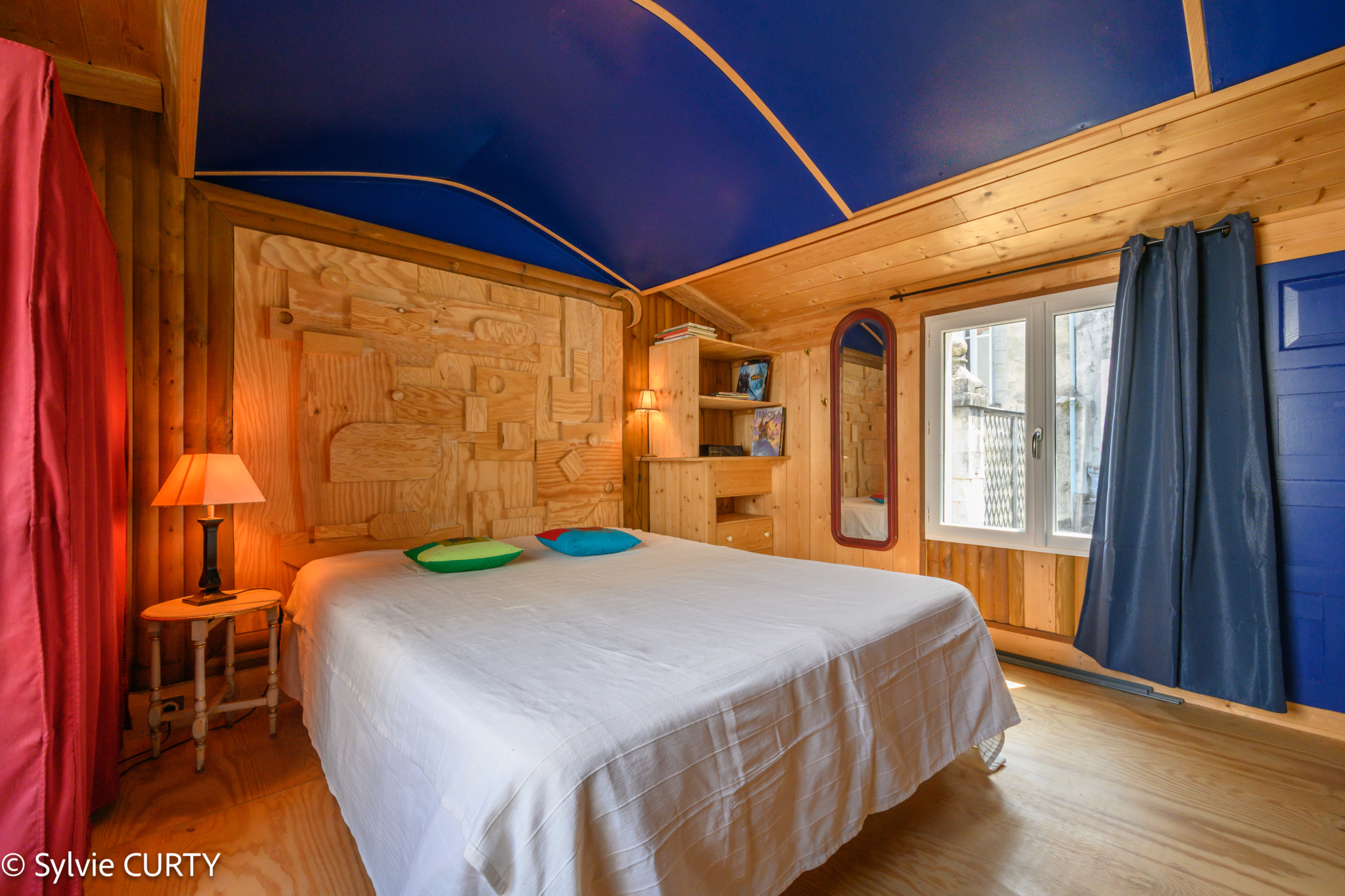 Chambre de caractère Chambre avec lit double, mur en bois et plafond bleu, fenêtres donnant sur l'extérieur.