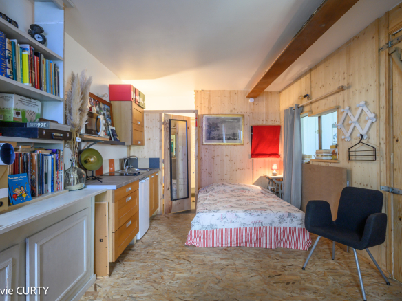 Intérieur d'une maison de caractère avec cuisine et coin nuit, murs en bois et décoration artistique.