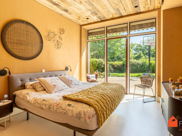 Chambre spacieuse avec lit double et accès à un jardin, murs en terre cuite et plafond en bois.