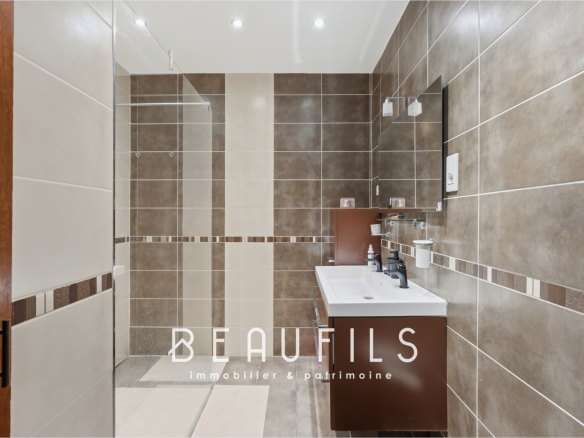 Modern bathroom with brown and beige tiled flooring, sink and mirror.