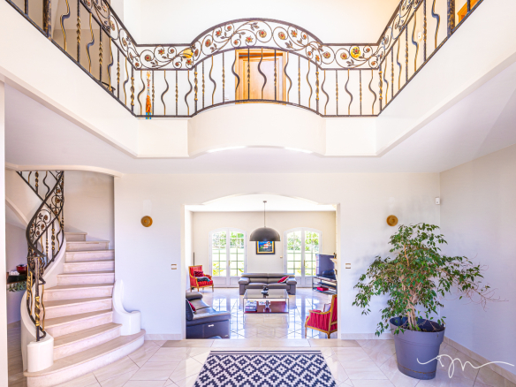 Intérieur d'une villa avec un hall d'entrée spacieux, escalier et salon lumineux.