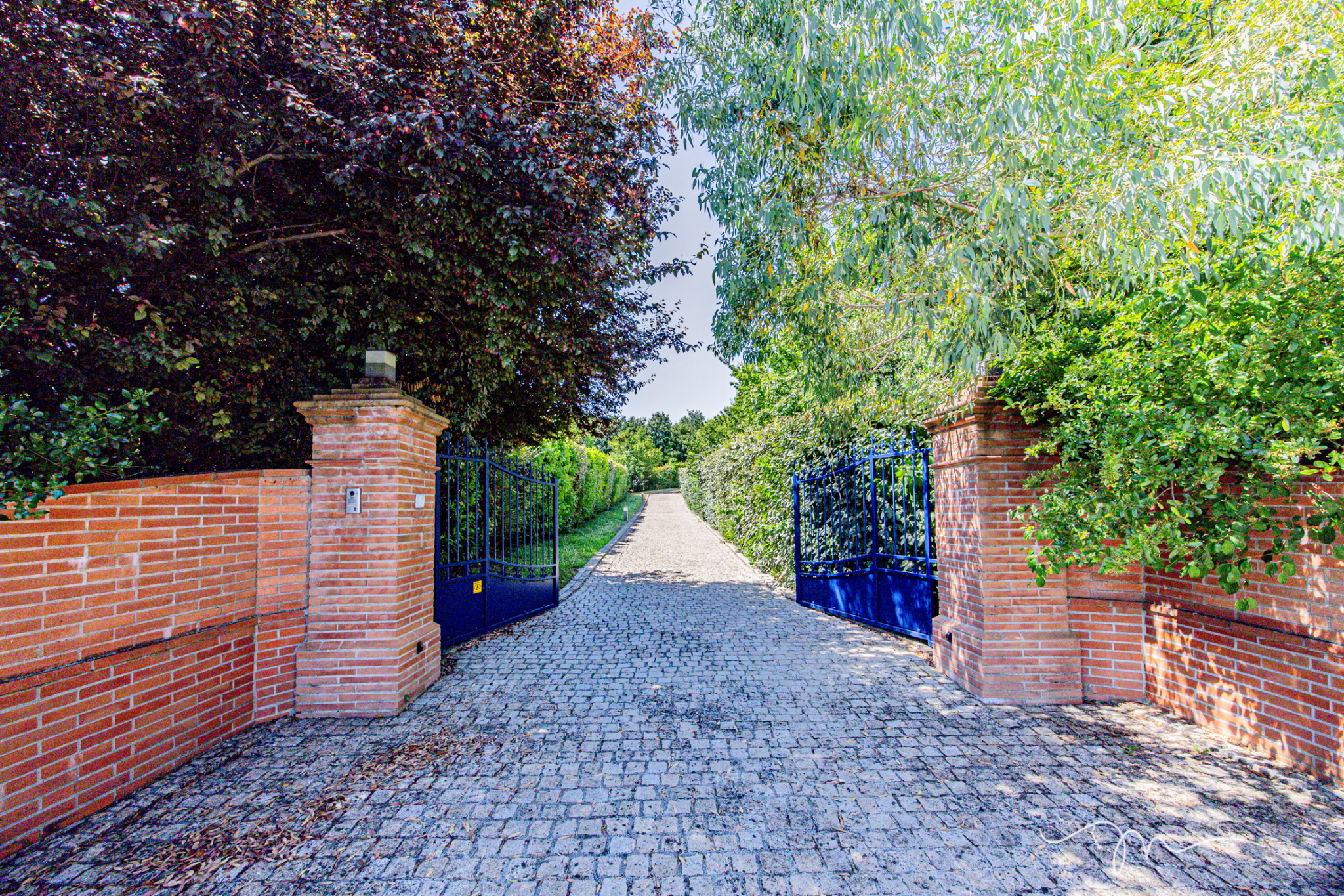 Entrée d'une villa avec portail bleu et chemin pavé, entourée de verdure à Préserville.