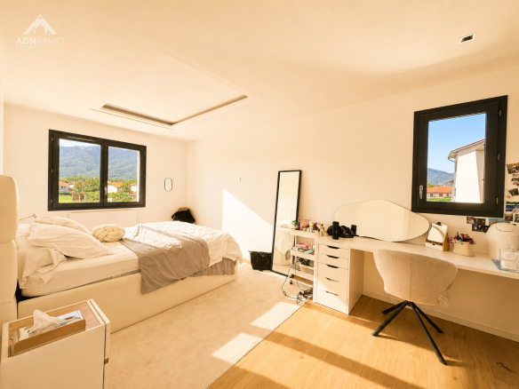 Chambre lumineuse avec lit, bureau et fenêtres sur un paysage montagneux.