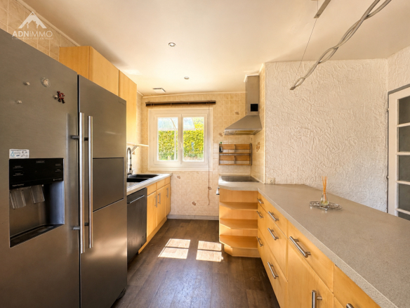 Cuisine moderne avec des équipements en bois et des grandes fenêtres laissant entrer la lumière.