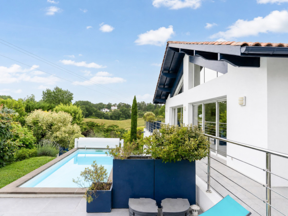 Vue de la piscine et de la maison moderne avec jardin à Urrugne, ensoleillée et verdoyante.