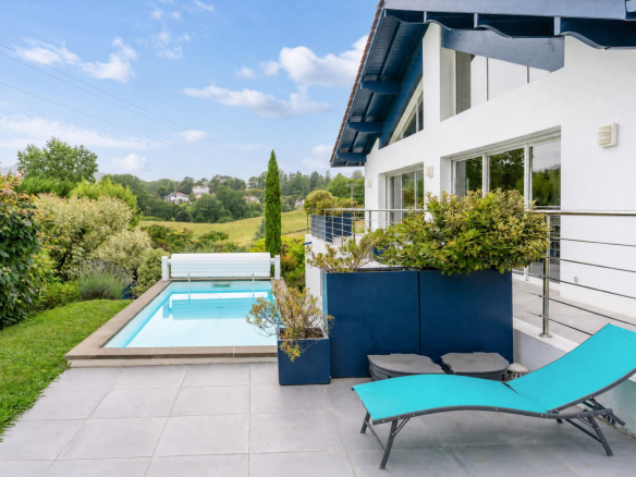 Vue de la piscine et de la terrasse d'une propriété familiale à Urrugne, avec jardin paysagé.