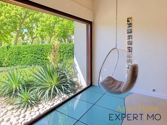 Interior of a modernist villa with a hanging chair and a view of the wooded garden.