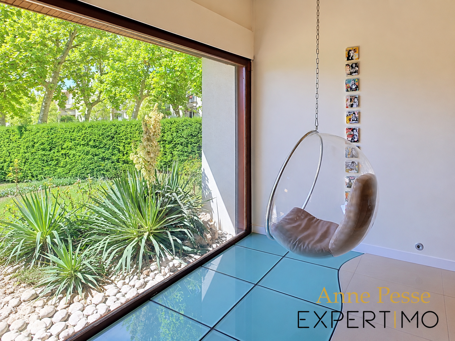 Interior of a modernist villa with a hanging chair and a view of the wooded garden.