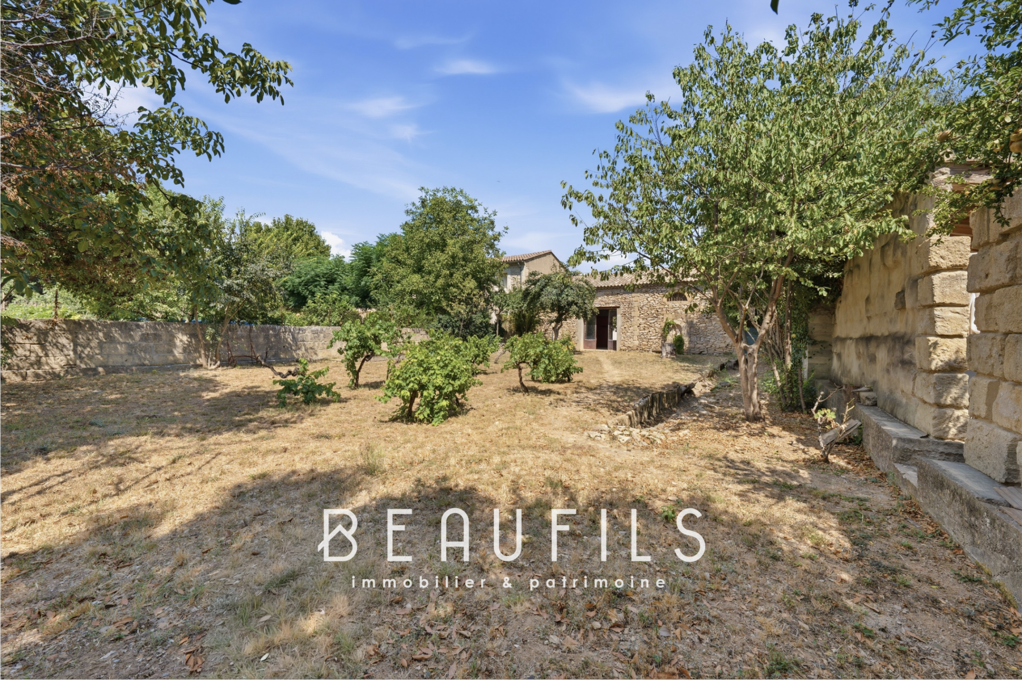Jardin d’une maison vigneronne à Vergèze Jardin paysager d'une maison de maître vigneronne à Vergèze, avec arbres et murs en pierre.
