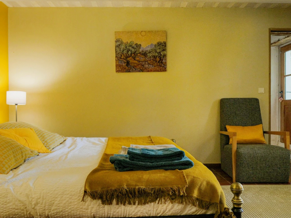 Chambre d'un mas rénové avec lit, fauteuil et décoration chaleureuse.