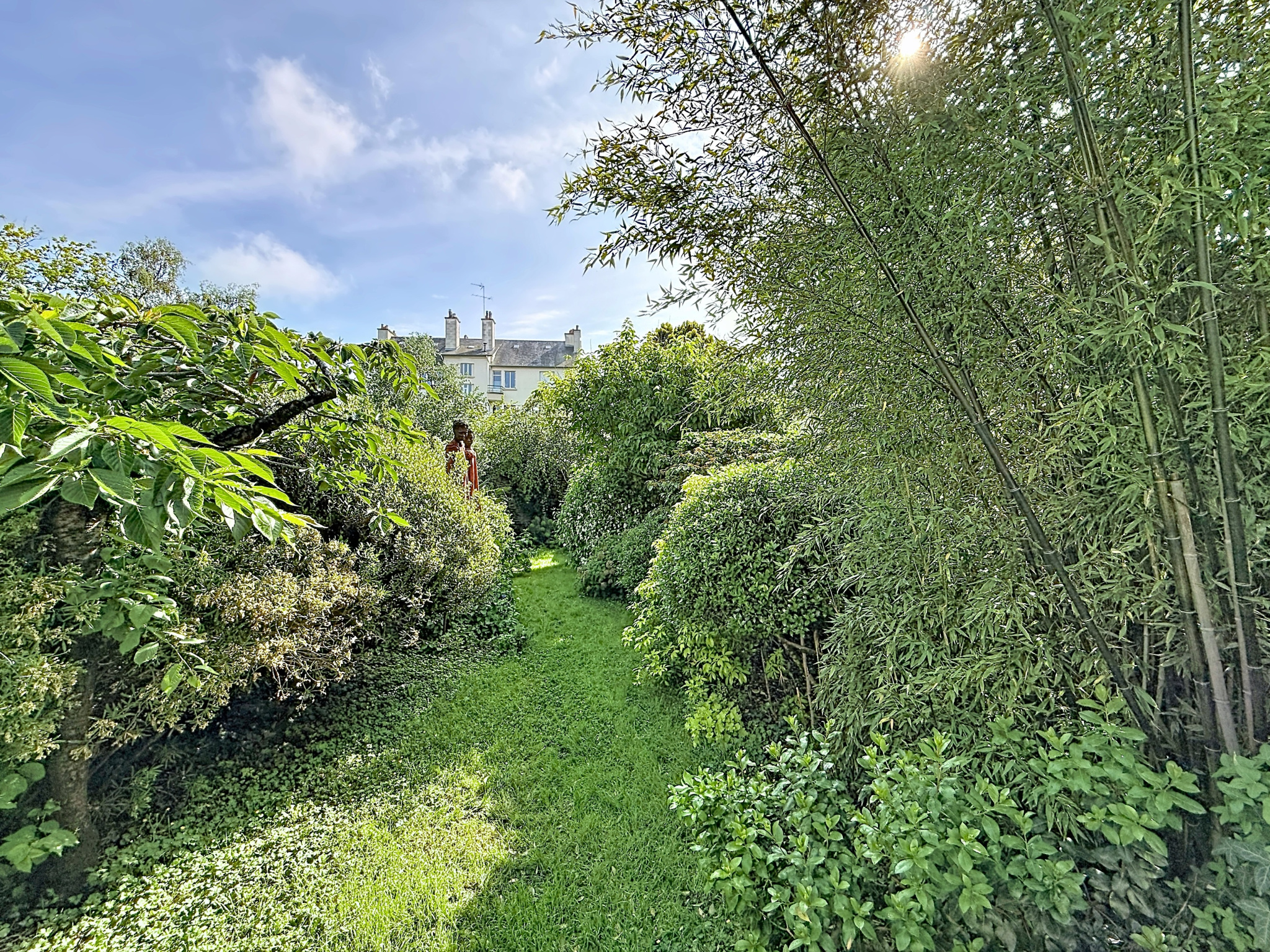 Jardin verdoyant avec des haies et des arbres, maison visible en arrière-plan, quartier Thabor à Rennes.