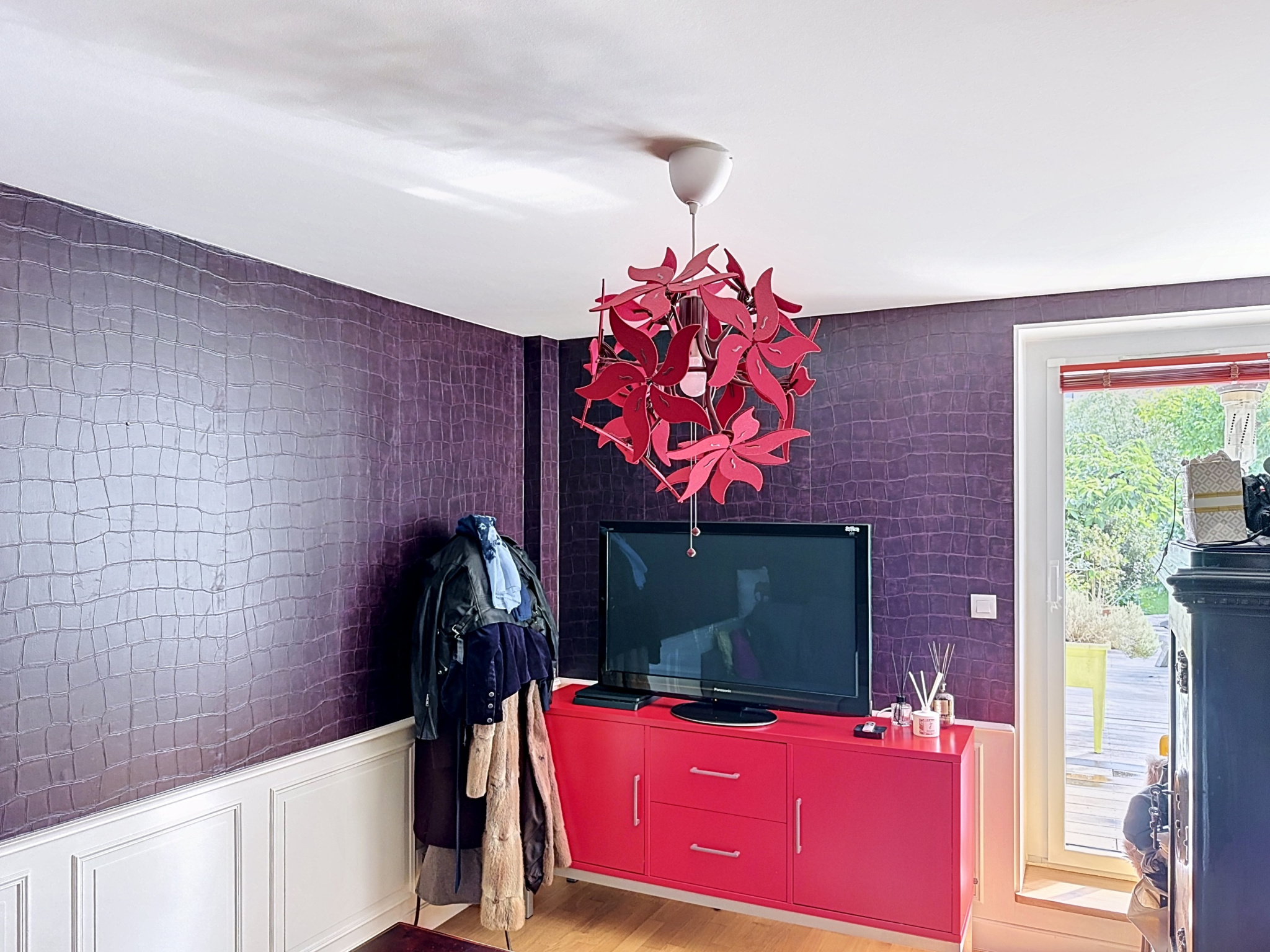 Intérieur d'une maison avec un salon, télévision et un lampadaire rouge, murs violets.