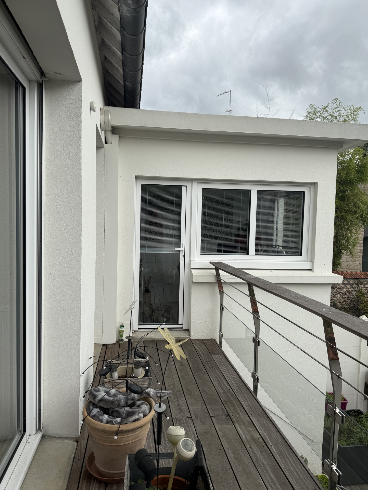 Balcon d'une maison moderne avec des pots de fleurs et un garde-corps en verre.